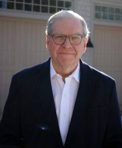 Joe Lockhart wearing a navy blazer and white shirt, standing outdoors in front of a building.